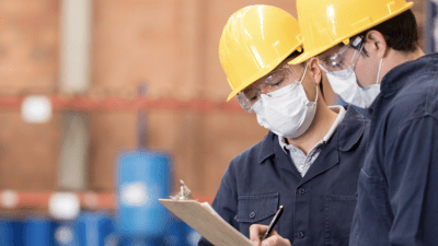 Two people in hard hats and face masks looking at a clipboard