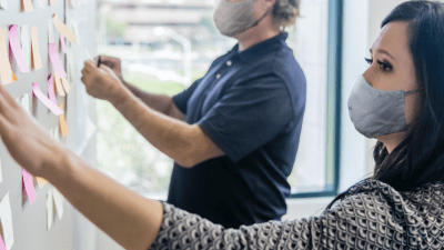 Man and woman in face masks putting Post-It notes on a whiteboard