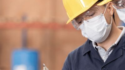 Two people in hard hats and face masks looking at a clipboard